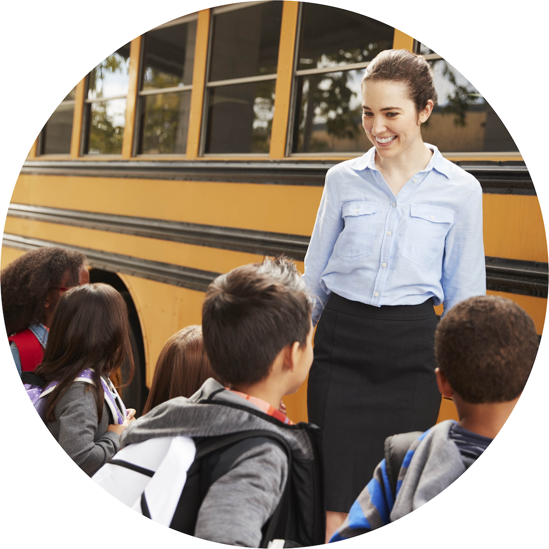 teacher with students besides a school bus